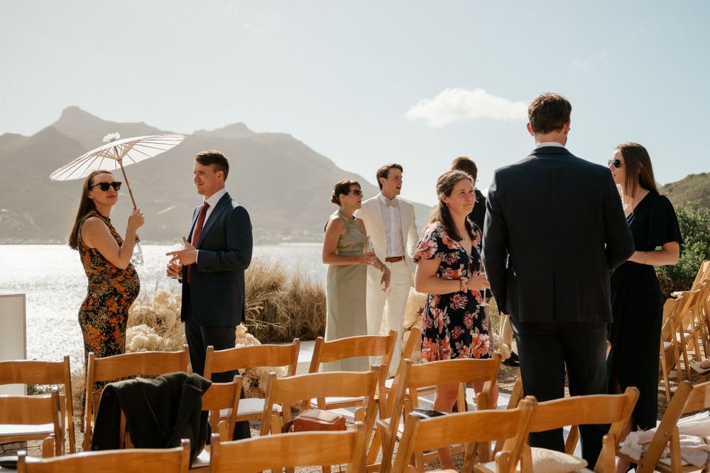Wedding guests mingle before the ceremony with mountain and ocean views in the background.