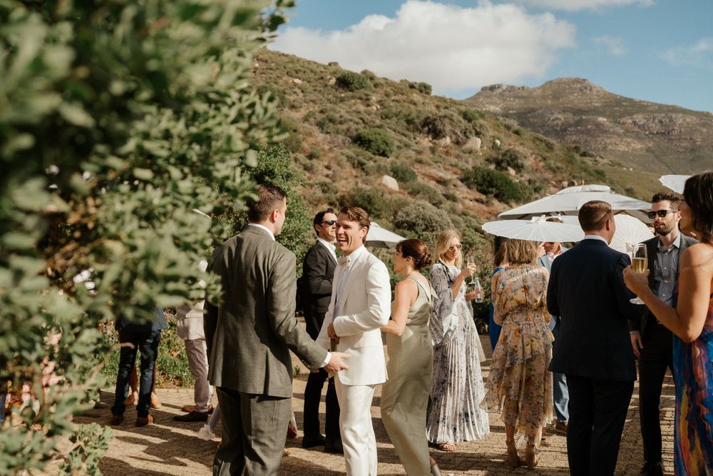 Wedding guests mingling at outdoor reception with mountains in background.
