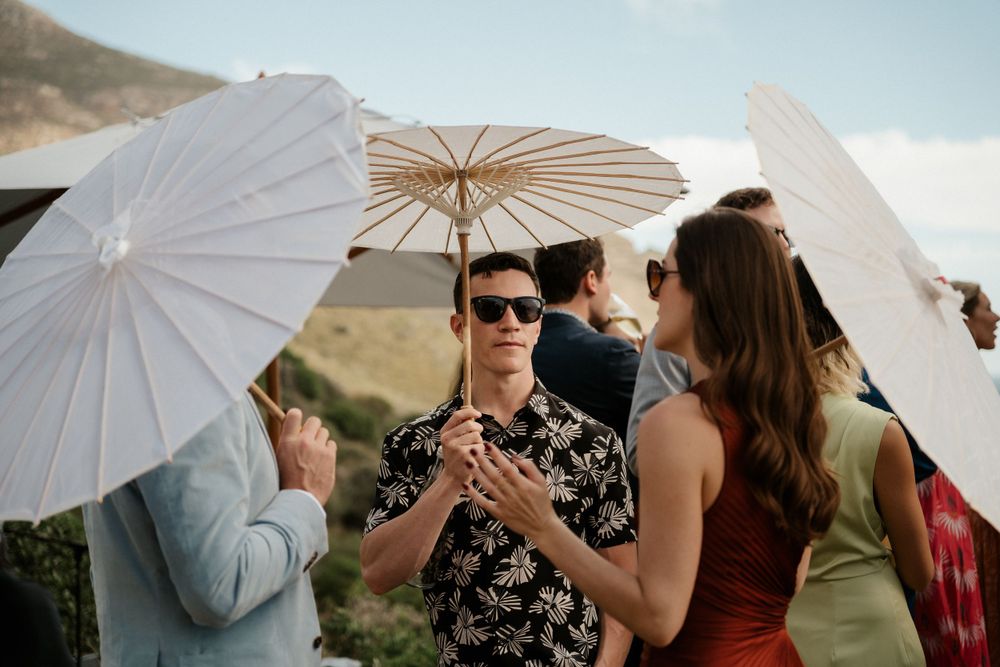 Guests mingling with white parasols at an outdoor mountain wedding reception.