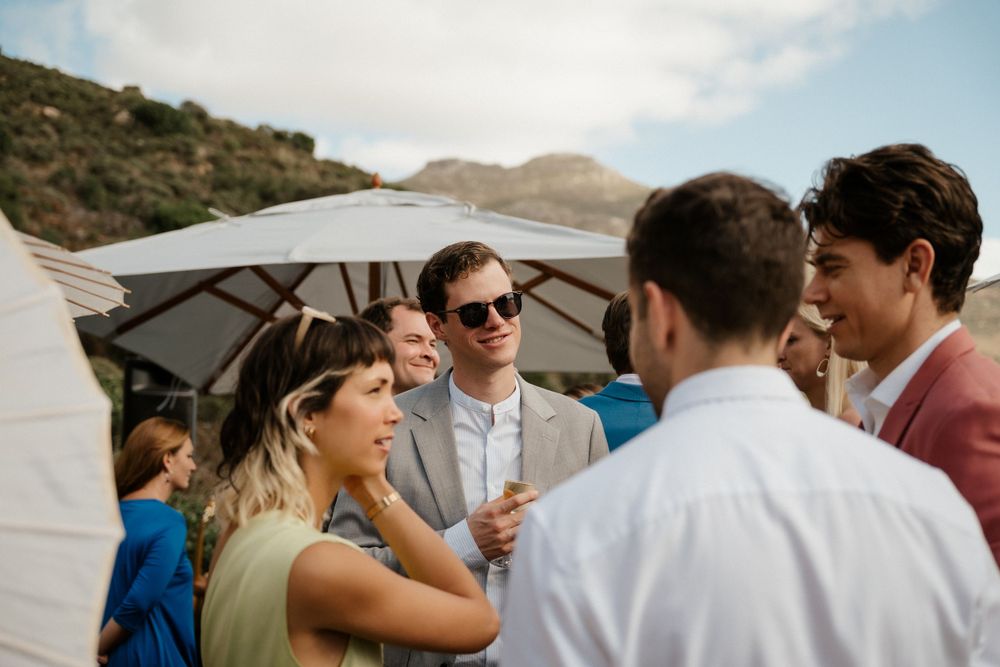 Wedding guests socializing under a patio umbrella at an outdoor reception.