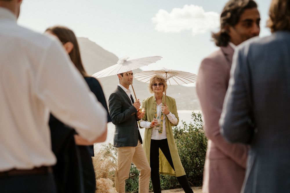 Guests enjoying drinks and conversation at outdoor wedding reception with parasols.