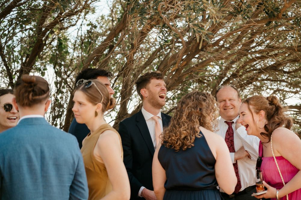 Wedding guests gather outdoors under trees during a celebratory moment.