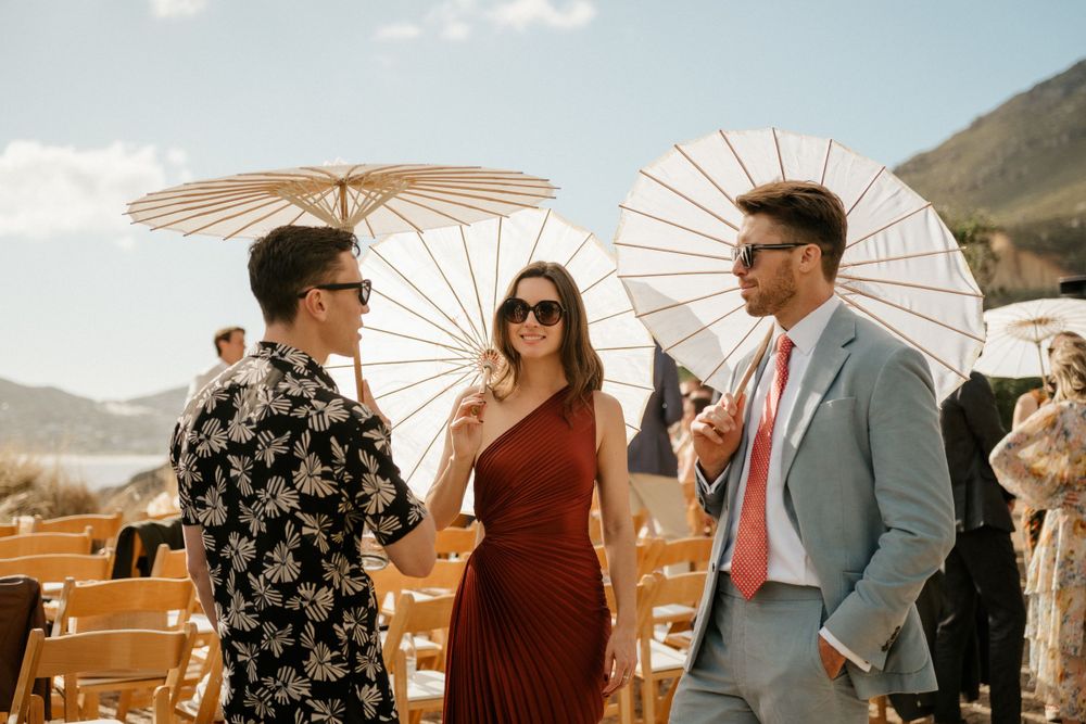 Guests chatting under paper parasols at a sunny outdoor wedding venue.