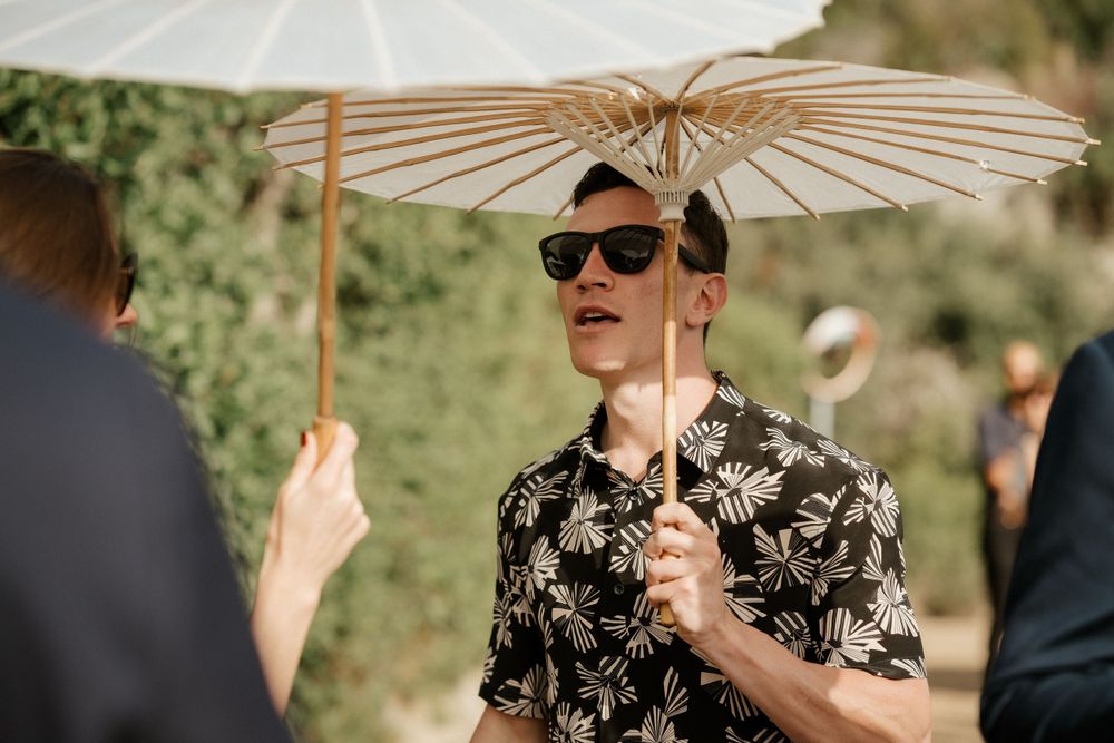 A guest holds a white paper parasol while enjoying the outdoor wedding festivities.