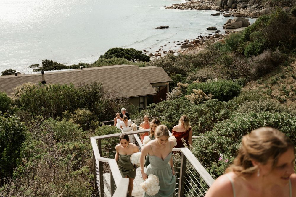 Wedding party descending outdoor stairs with coastal views in the background.