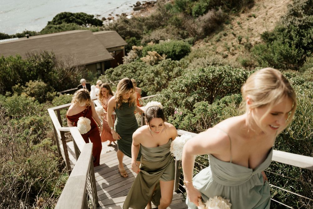Group walking down outdoor stairs at coastal venue in summer dresses.