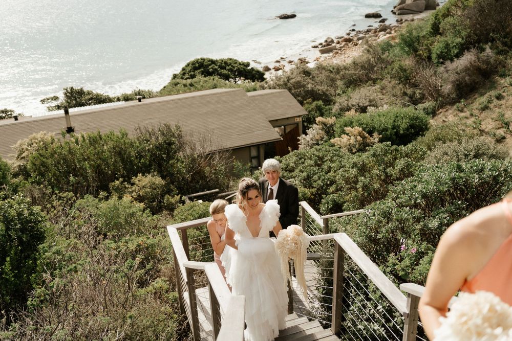 A couple descends white coastal stairs with ocean views during their wedding day.