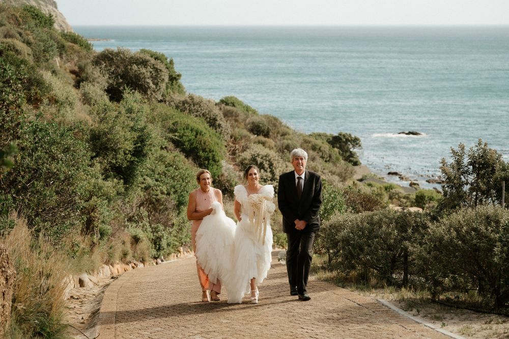Three people walking down a coastal path with ocean views during a wedding celebration.