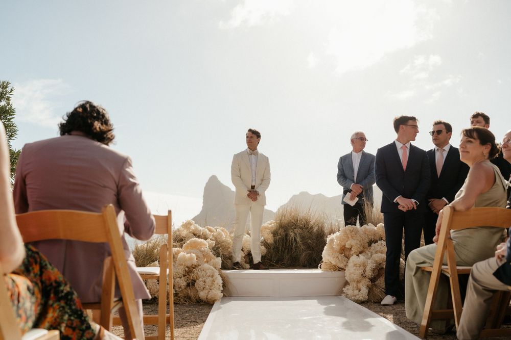 Sunny outdoor wedding ceremony setup with hay bale seating and mountain backdrop.