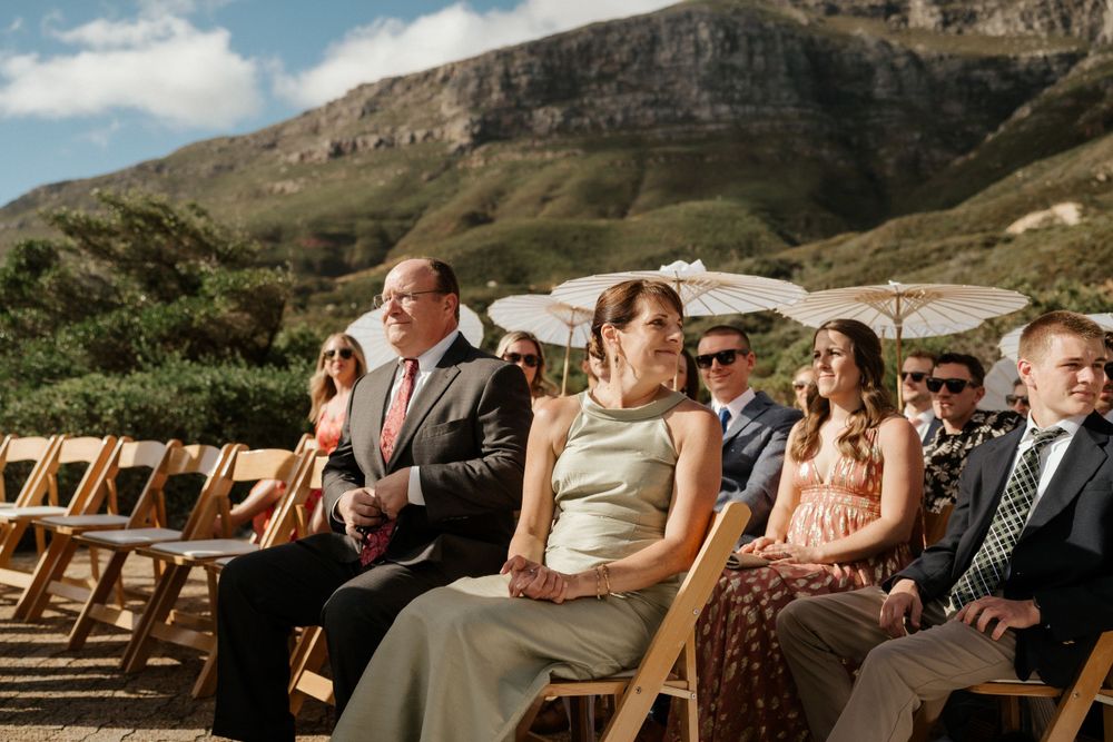 Outdoor wedding ceremony with guests seated against a dramatic mountain backdrop.