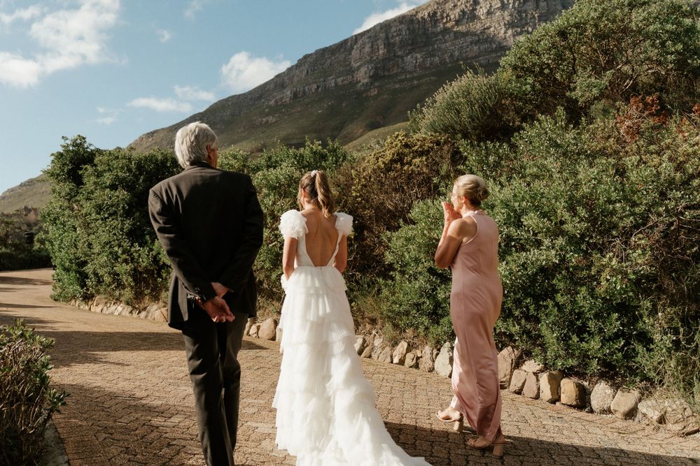 A wedding ceremony processional on a scenic mountain path with attendants in formal attire.