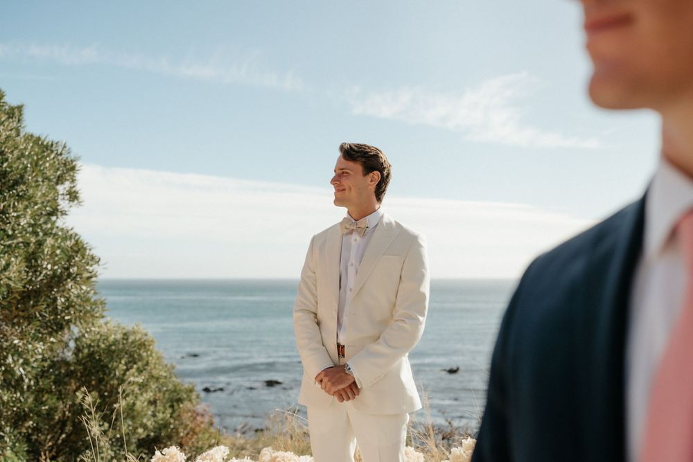 A seaside wedding ceremony with attendees in formal attire against an ocean backdrop.