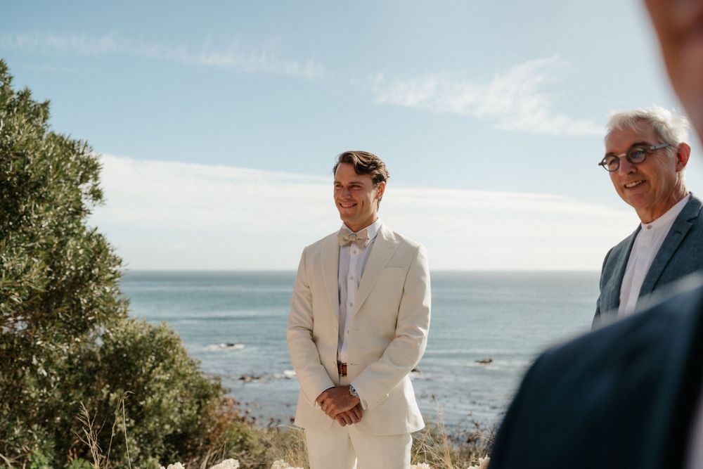 Seaside wedding ceremony with attendees standing against ocean backdrop.