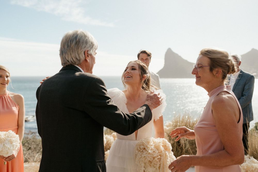 Joyful outdoor wedding ceremony moment with ocean and cliffs in the background.
