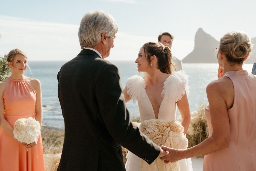 Intimate oceanside wedding ceremony with coastal rock formations visible in the background.