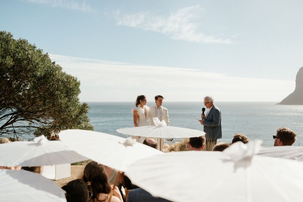 Intimate coastal wedding ceremony overlooking the ocean with white decor and natural scenery.
