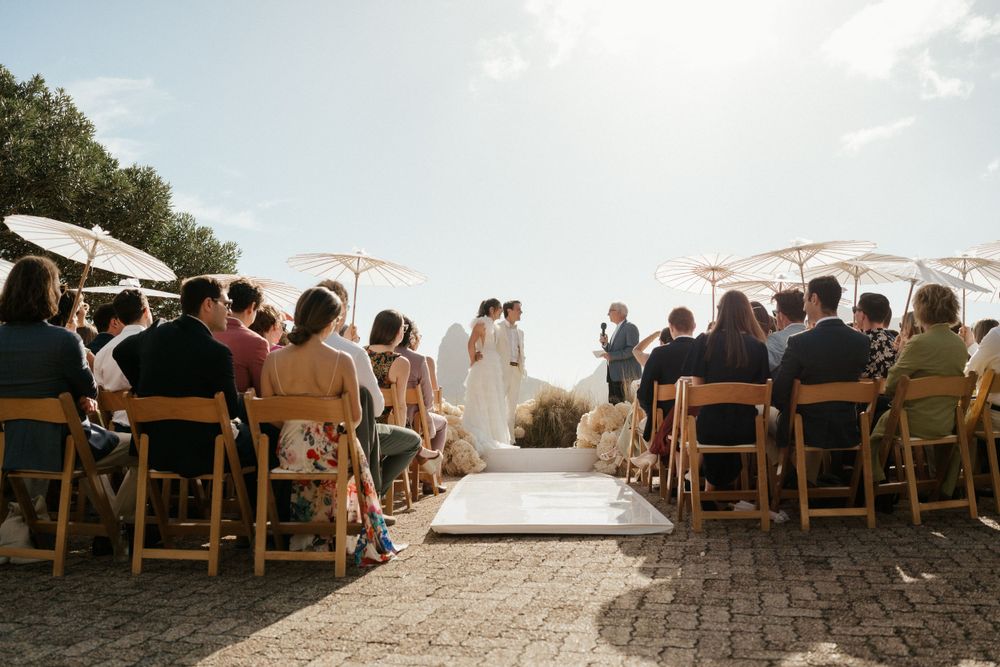 Wedding ceremony setup with white parasols and wooden chairs facing an ocean view.