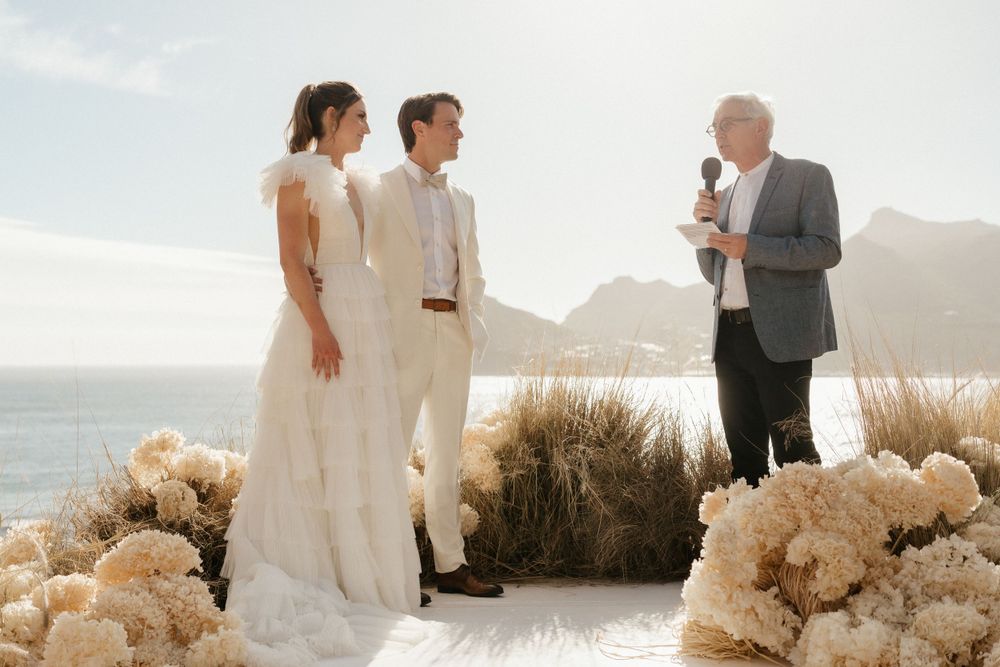 A seaside wedding ceremony with floral arrangements and stunning coastal mountain backdrop.