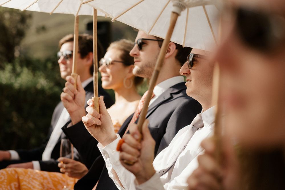Guests holding decorative white parasols during an outdoor celebration.