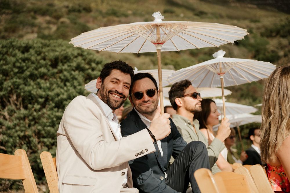Wedding guests sharing laughs under white parasols at an outdoor celebration.