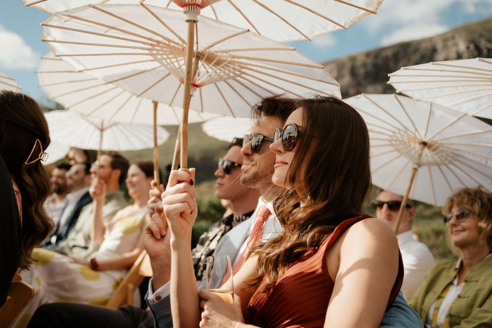 Wedding guests holding white parasols while enjoying an outdoor celebration.