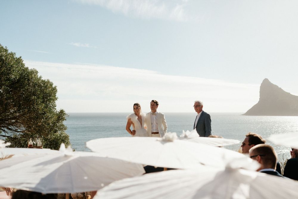A scenic coastal wedding ceremony with white parasols and ocean views.