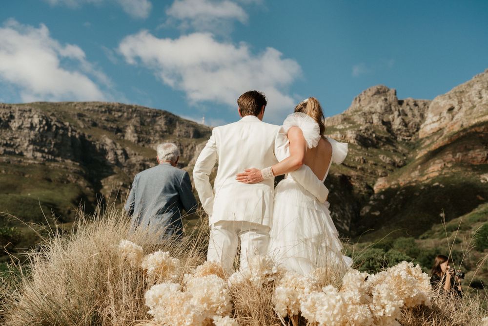 A wedding party stands together against a backdrop of dramatic mountain peaks and golden grass.