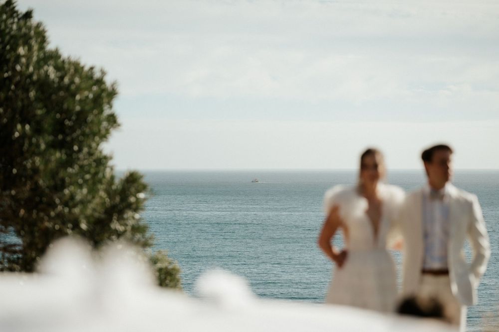 Soft focus coastal wedding scene with ocean view and figures silhouetted against the bright horizon.