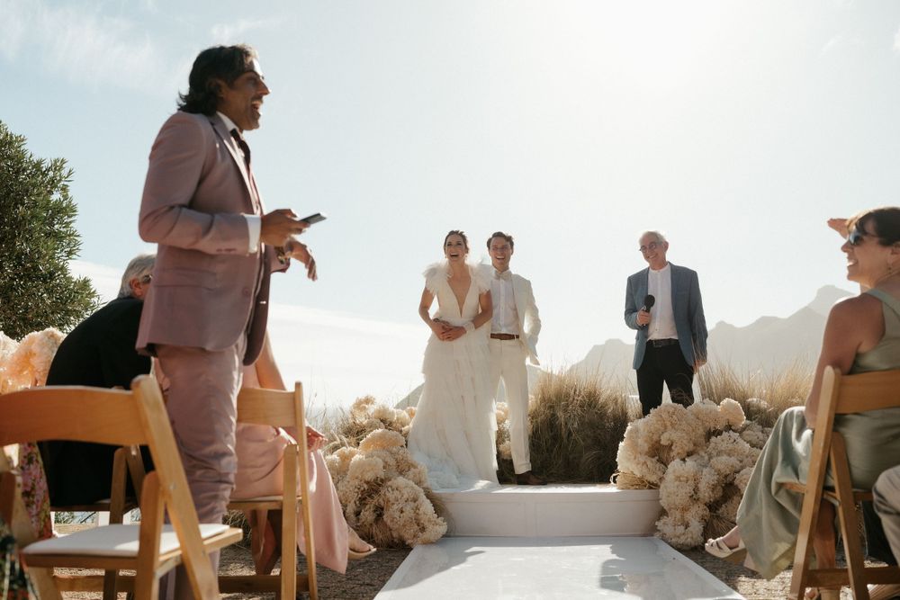 Wedding ceremony taking place outdoors with mountain scenery and golden sunlight filtering through.