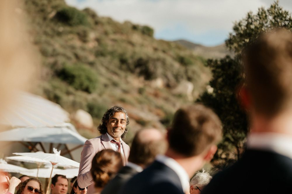 Speech being given at an outdoor wedding with hillside and parasols visible.