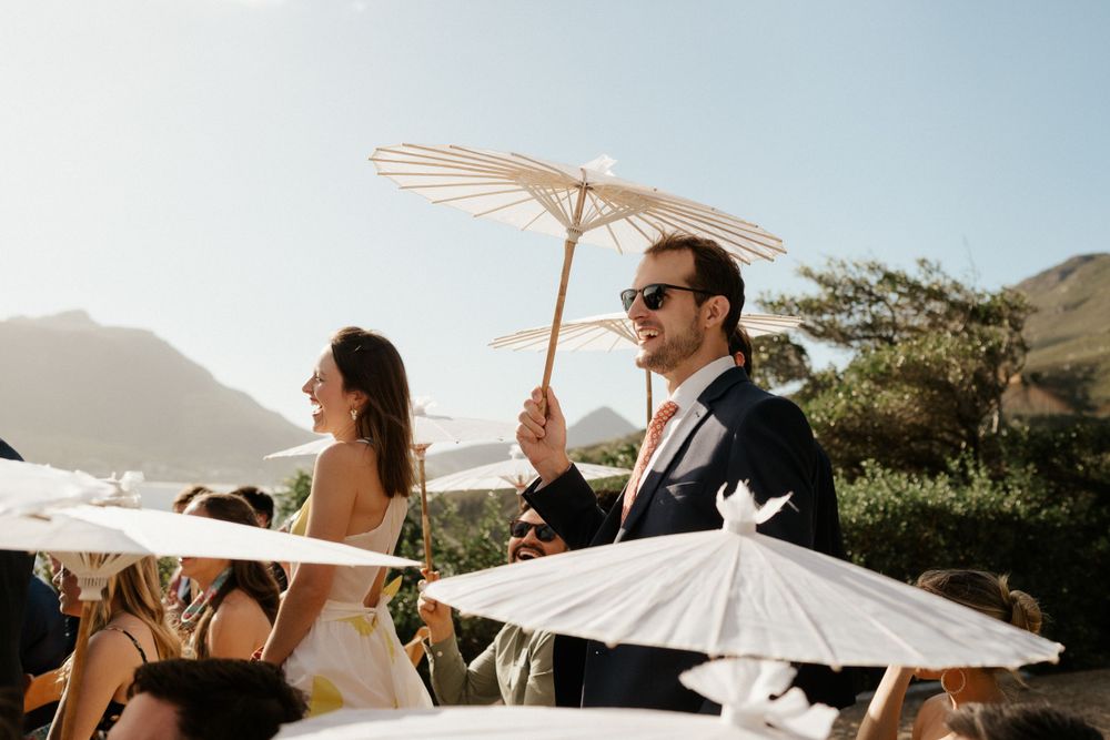 Outdoor wedding celebration with white parasols against a mountainous backdrop.