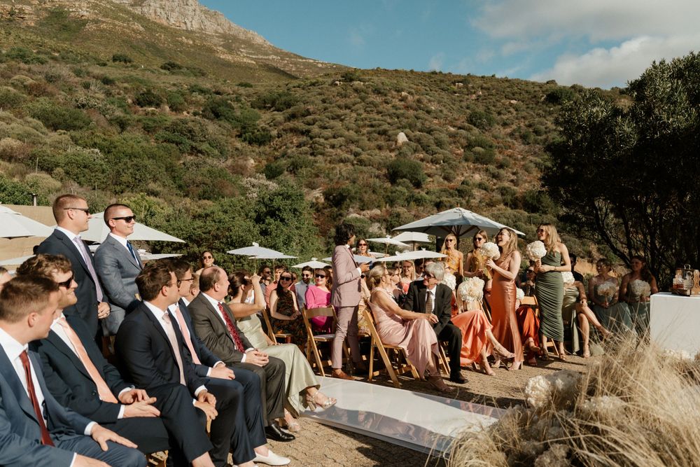 Wedding guests seated on tiered stone seating overlooking a mountainous coastal landscape.