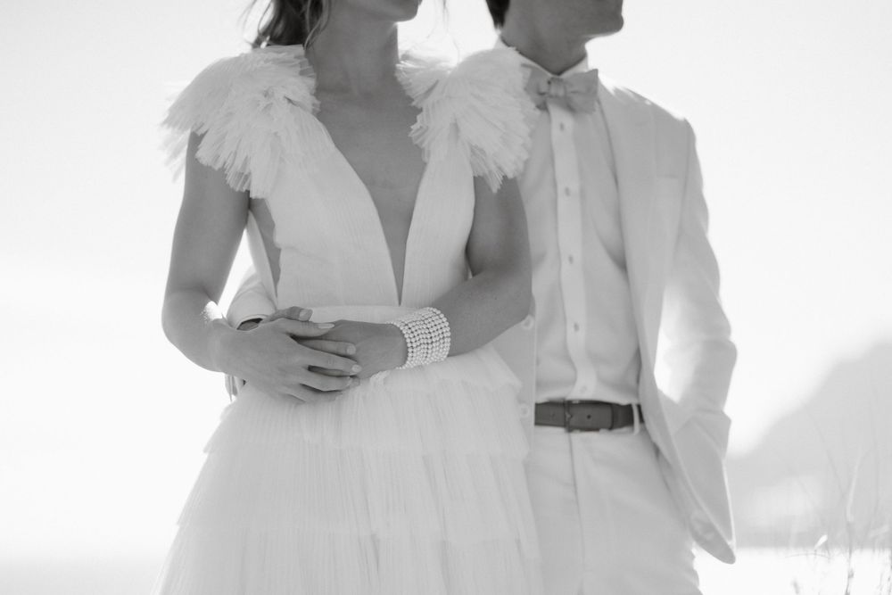 A black and white photograph captures an intimate moment in elegant white wedding attire.