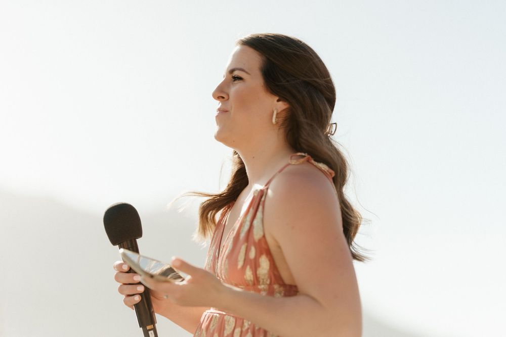 Person in pink dress speaking into microphone against white background.