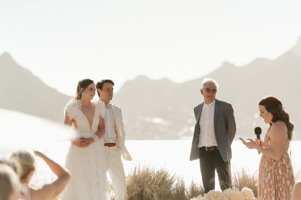 Wedding ceremony by the ocean with mountain views and floral arrangements at sunset.