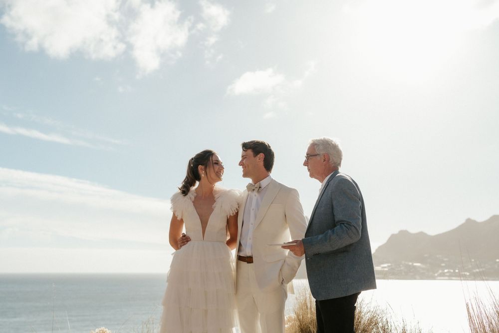 Coastal wedding ceremony overlooking ocean cliffs on sunny day.