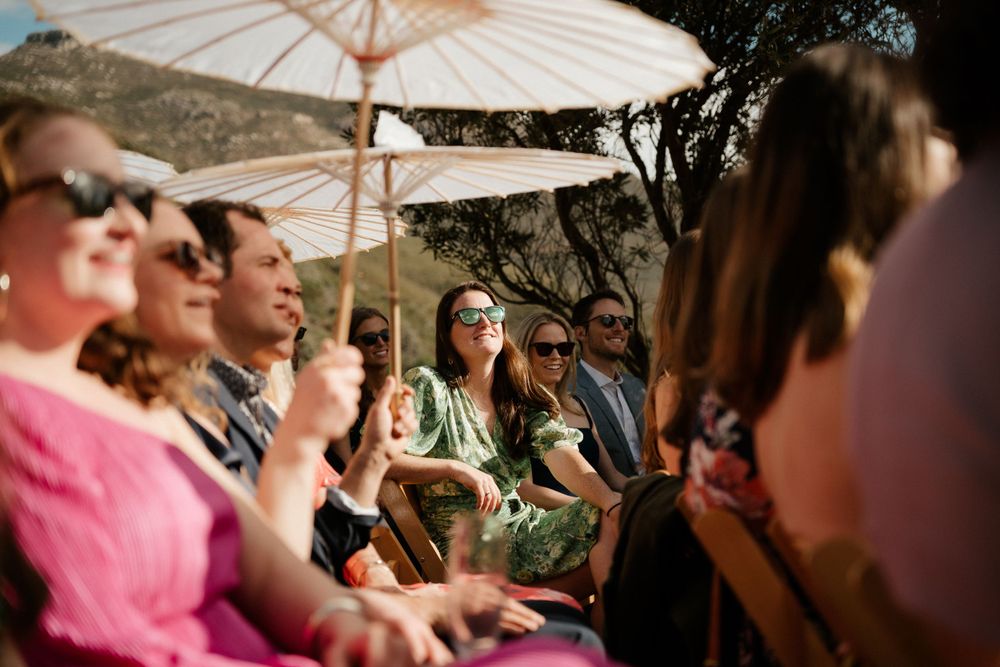 Wedding guests enjoying the celebration under parasol umbrellas in the afternoon sun.