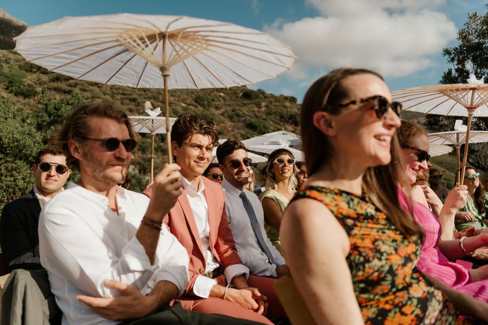 Wedding guests seated outdoors under white parasols enjoying the ceremony.