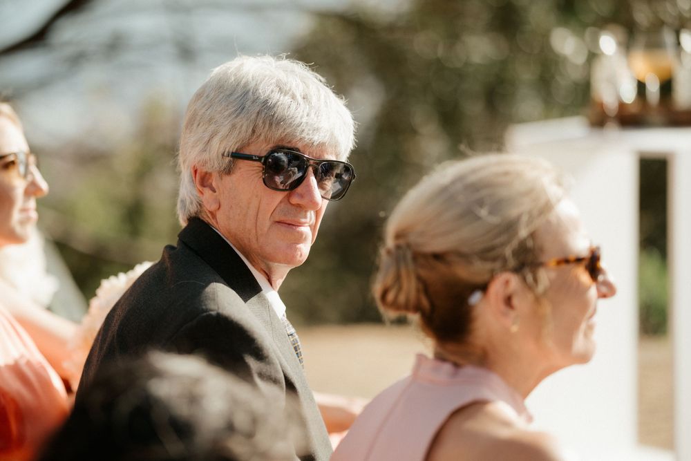 Wedding guest in dark sunglasses and formal attire at outdoor reception.
