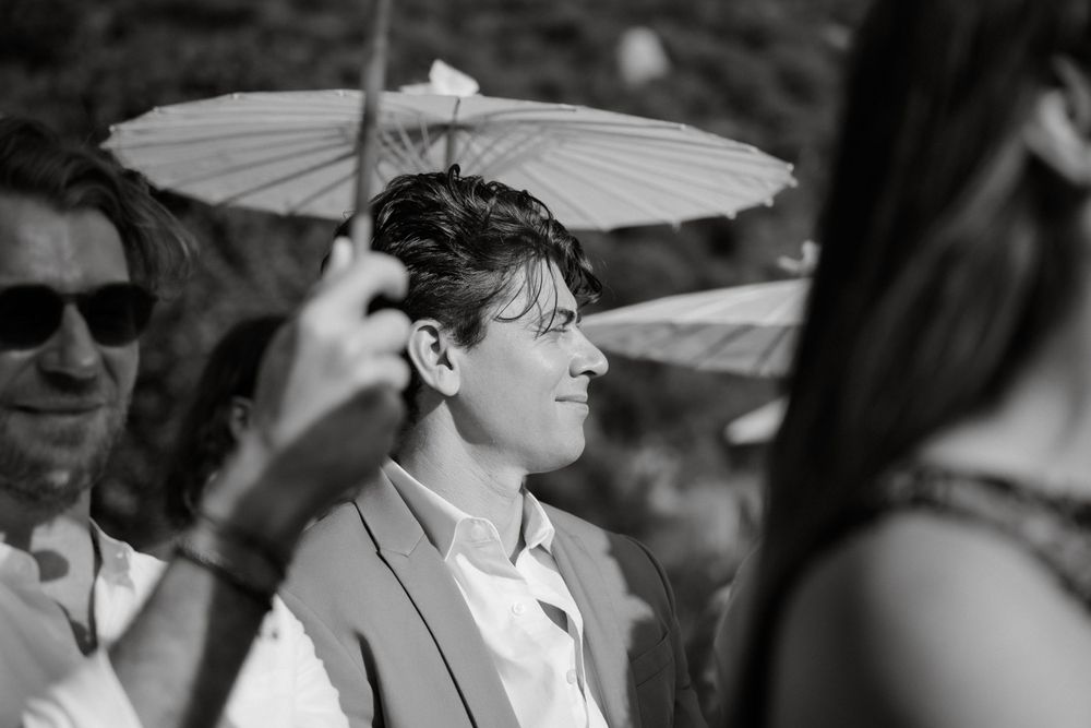 A guest shades themselves with a white paper parasol at an outdoor celebration.