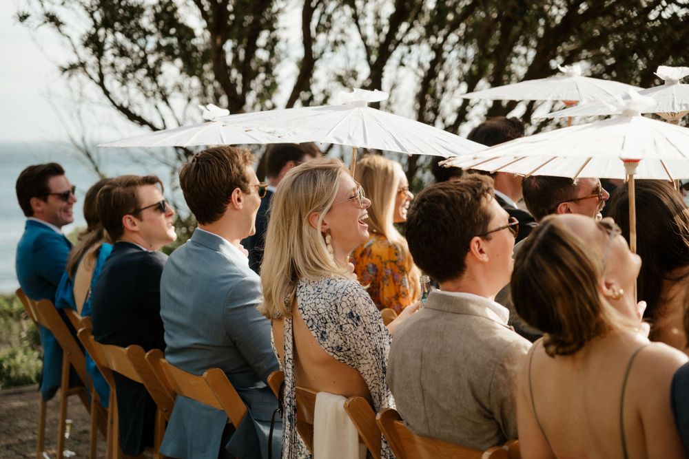 Guests seated in wooden chairs with parasols at an outdoor celebration overlooking the ocean.