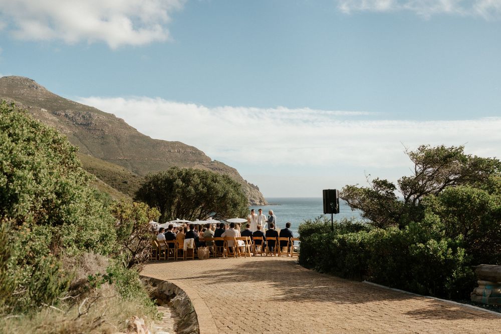 Wedding guests seated at outdoor reception with mountain and ocean views.