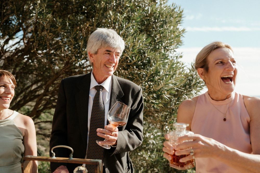 Wedding guests enjoying drinks and conversation at sunny outdoor reception.