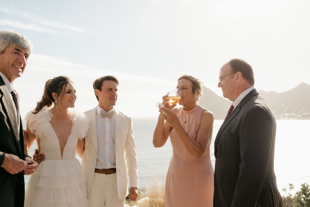 Wedding party enjoying drinks during outdoor celebration with ocean view.