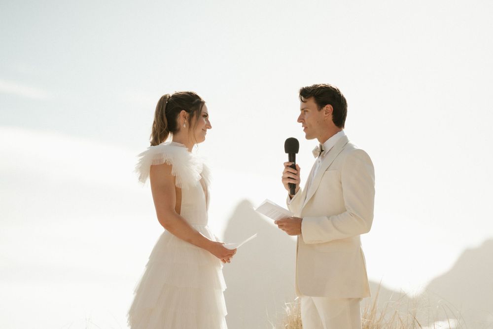 Couple exchanging vows during seaside wedding ceremony in white attire.