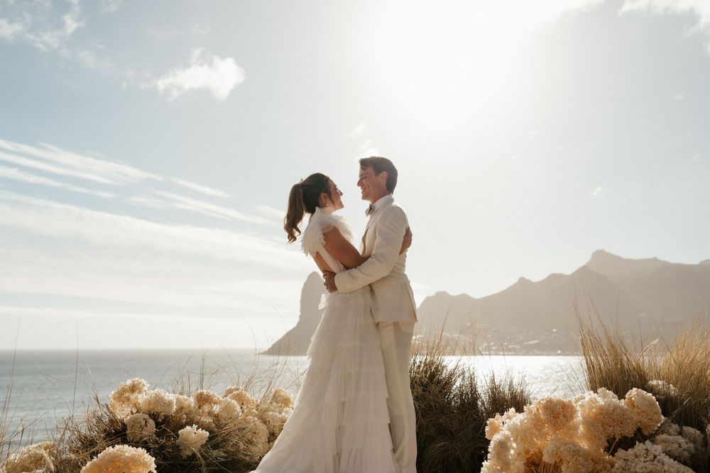 A romantic wedding moment silhouetted against mountain and ocean views at sunset.