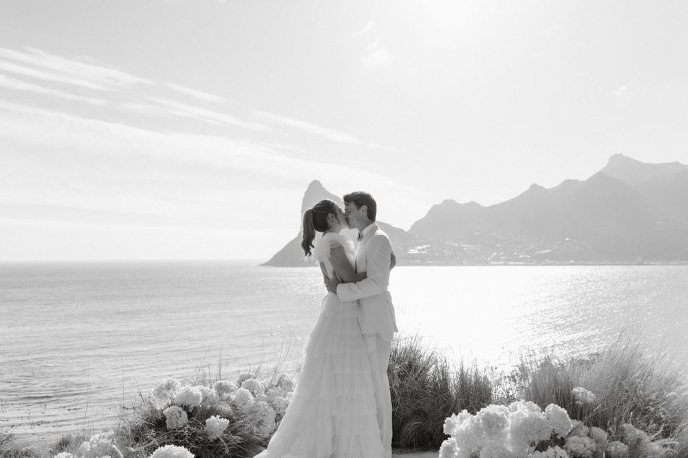 A romantic coastal wedding portrait with dramatic mountain and ocean views.