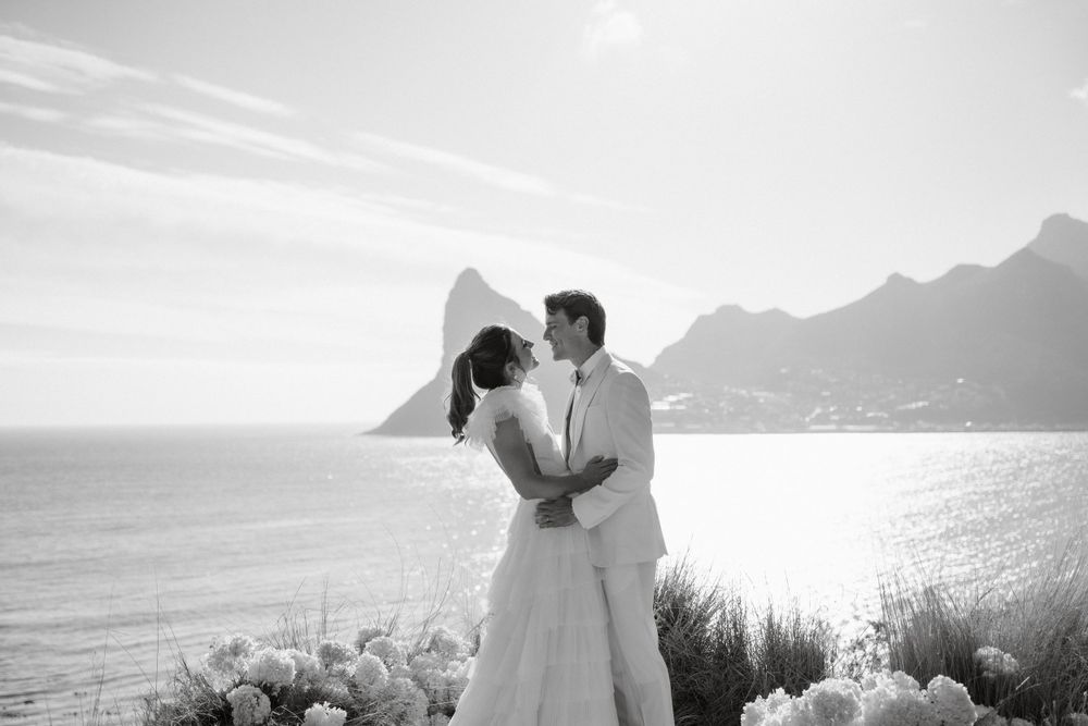 Romantic coastal wedding scene with mountains and ocean in the background.