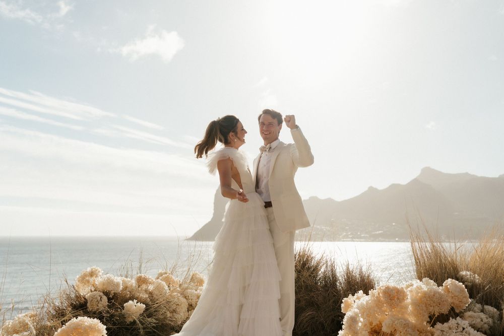 Couple dancing against ocean backdrop with dried floral arrangements at sunset.