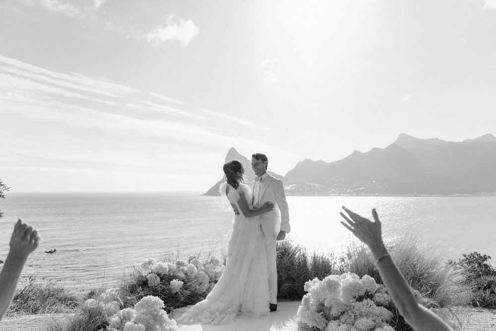 Black and white photo of a wedding celebration overlooking a dramatic coastal landscape.